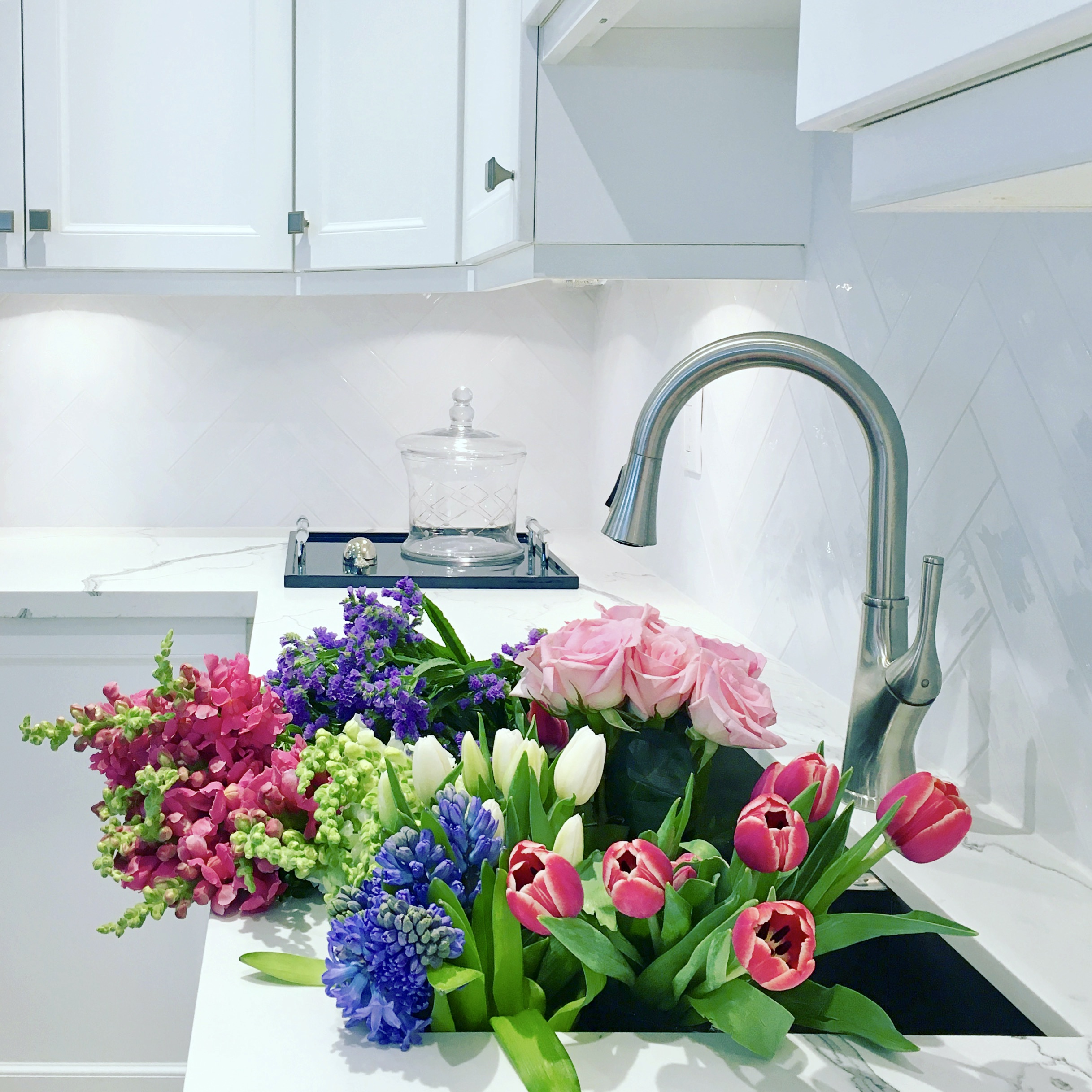 Kitchen interior designed by Fernanda Cunha Interiors, featuring white cabinets and showing a sink full of various colourful flowers
