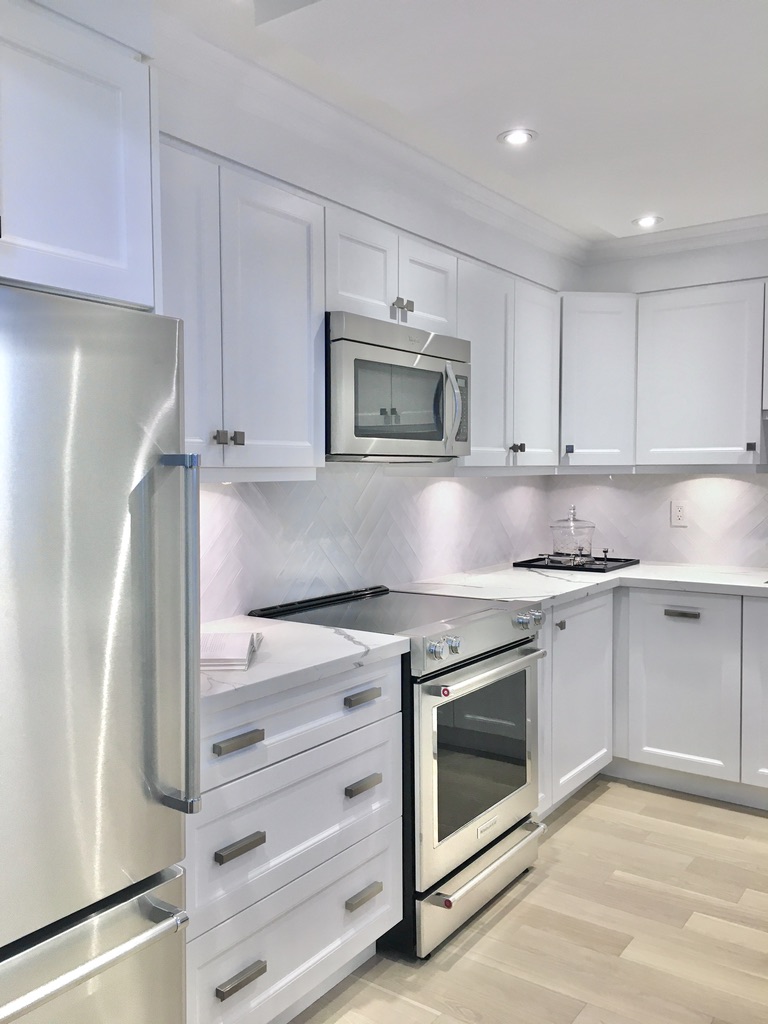 Kitchen designed by Fernanda Cunha Interiors featuring white cabinets, stainless steel appliances, white tile backsplash