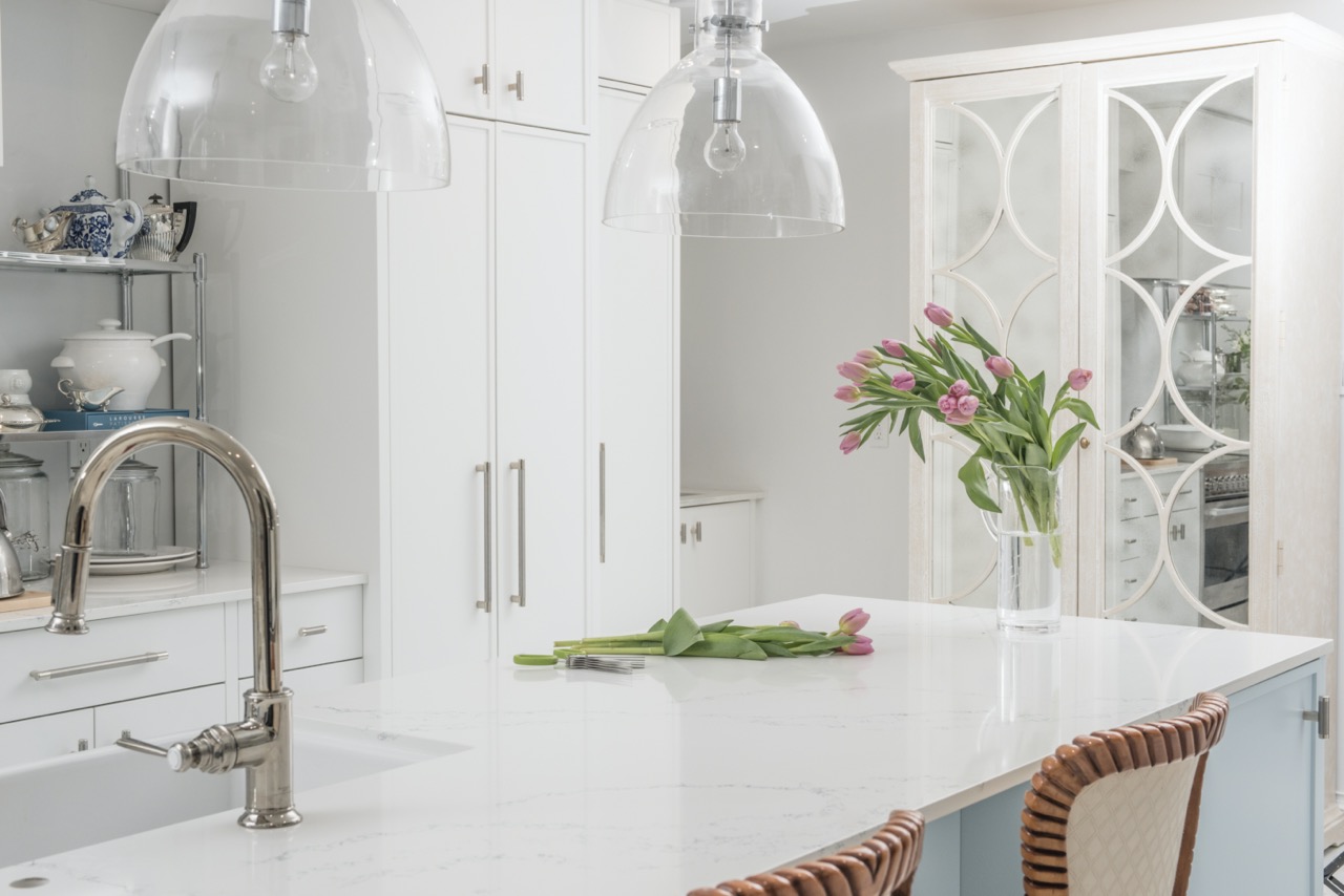 Kitchen designed by Fernanda Cunha Interiors, showing white kitchen cabinets and light blue kitchen island , with a vase with tulips